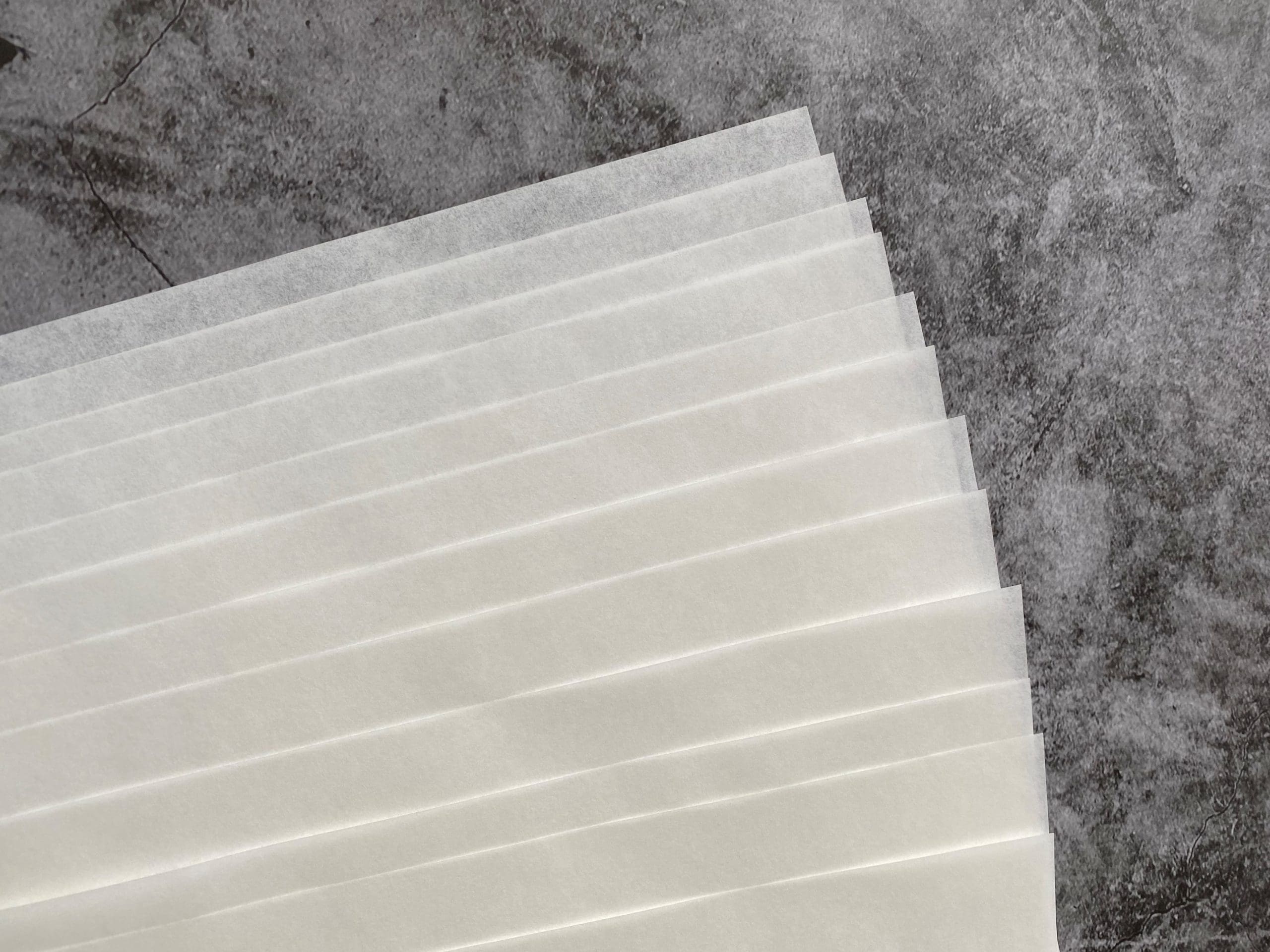 Stack of greaseproof baking paper sheets on a grey textured background.