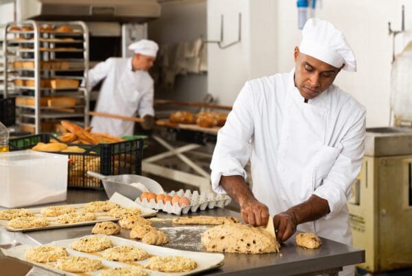Bakery staff in a commercial kitchen preparing dough and pastries on trays, highlighting baking process and food craftsmanship.