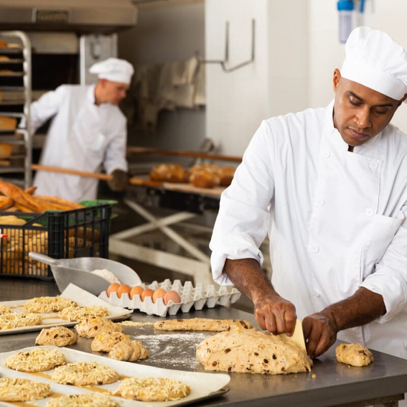 Professional bakers in a commercial bakery preparing dough and bread loaves.