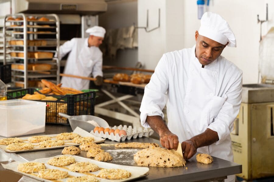 Professional bakers in a commercial bakery preparing dough and bread loaves.