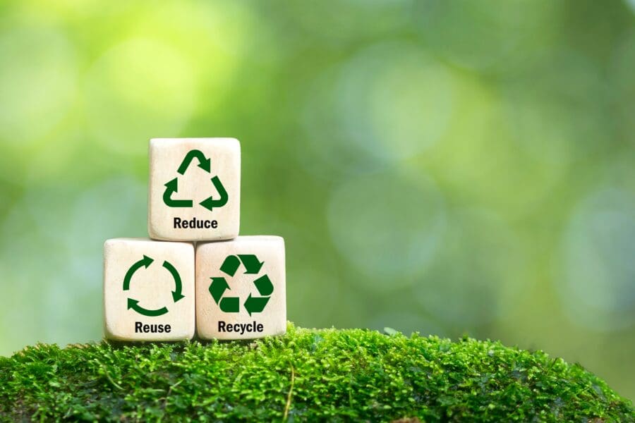 Sustainable Baker - Wooden blocks with reduce, reuse, and recycle symbols on moss with a blurred green background.