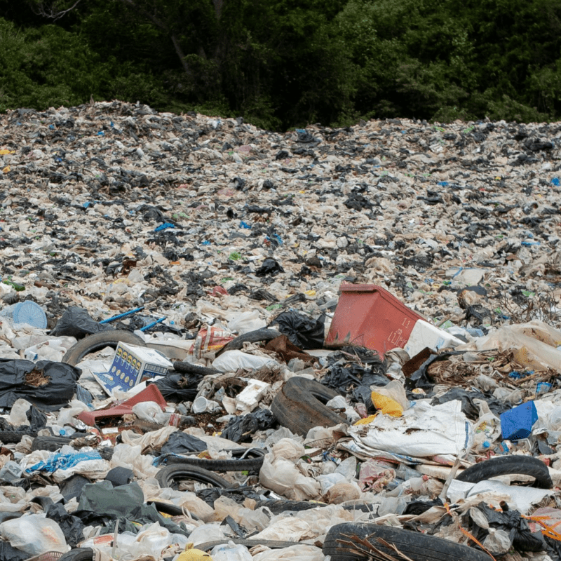 Large landfill site overflowing with plastic waste, bags, and mixed rubbish piled high.