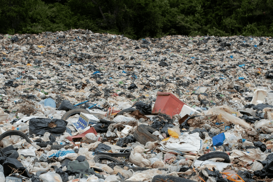 Large landfill site overflowing with plastic waste, bags, and mixed rubbish piled high.