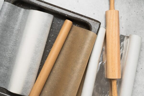 Rolls of baking paper, parchment, and foil with a wooden rolling pin and tray, essential for cooking and baking preparation.