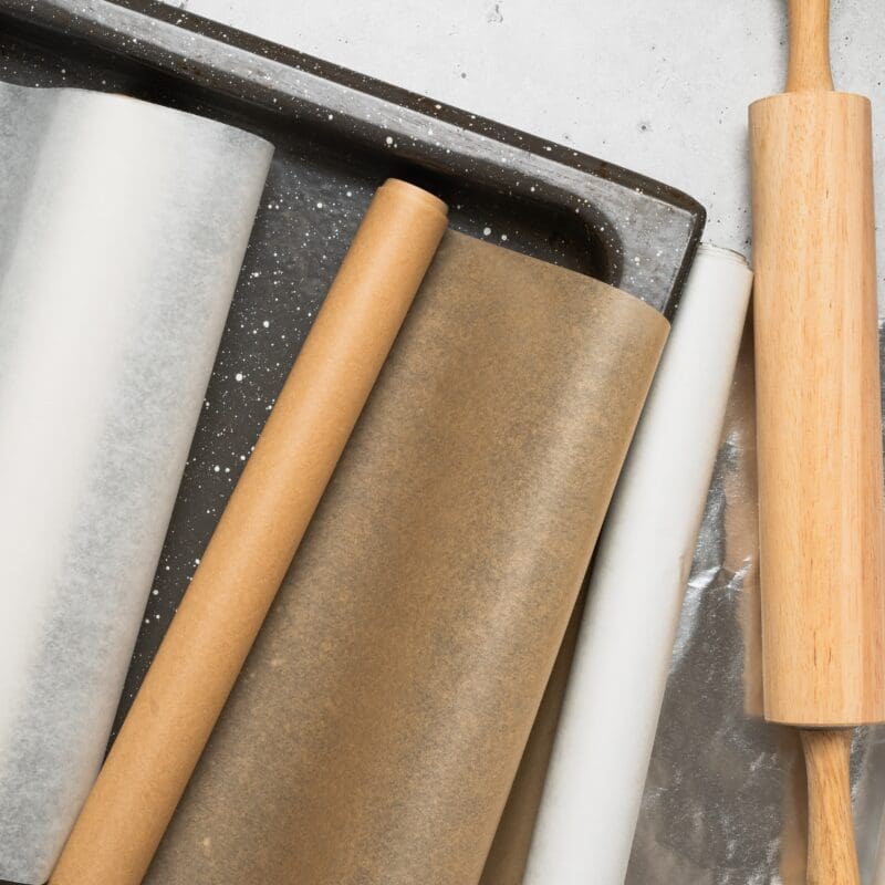 Rolls of baking paper, parchment, and foil with a wooden rolling pin and tray.