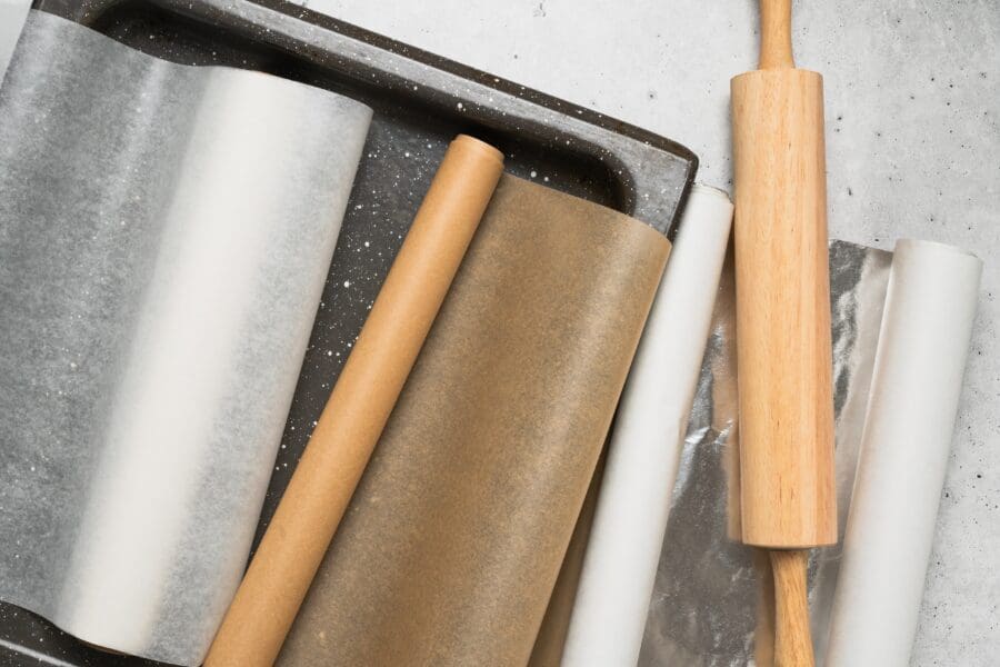 Rolls of baking paper, parchment, and foil with a wooden rolling pin and tray.