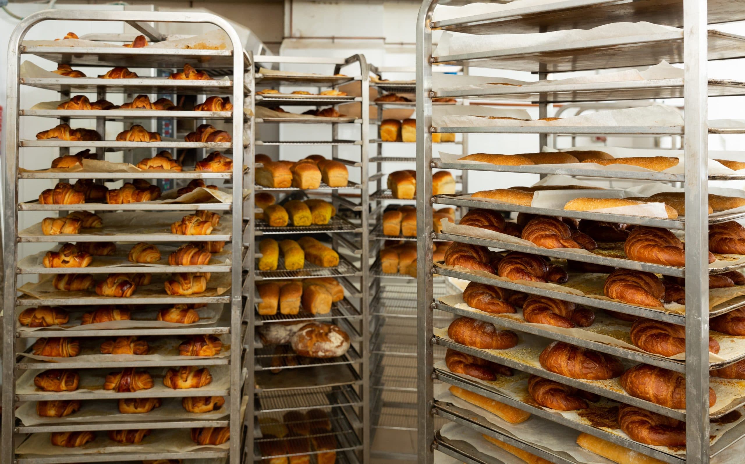 Metal bakery racks filled with freshly baked croissants, pastries, rolls and loaves in a commercial bakery.